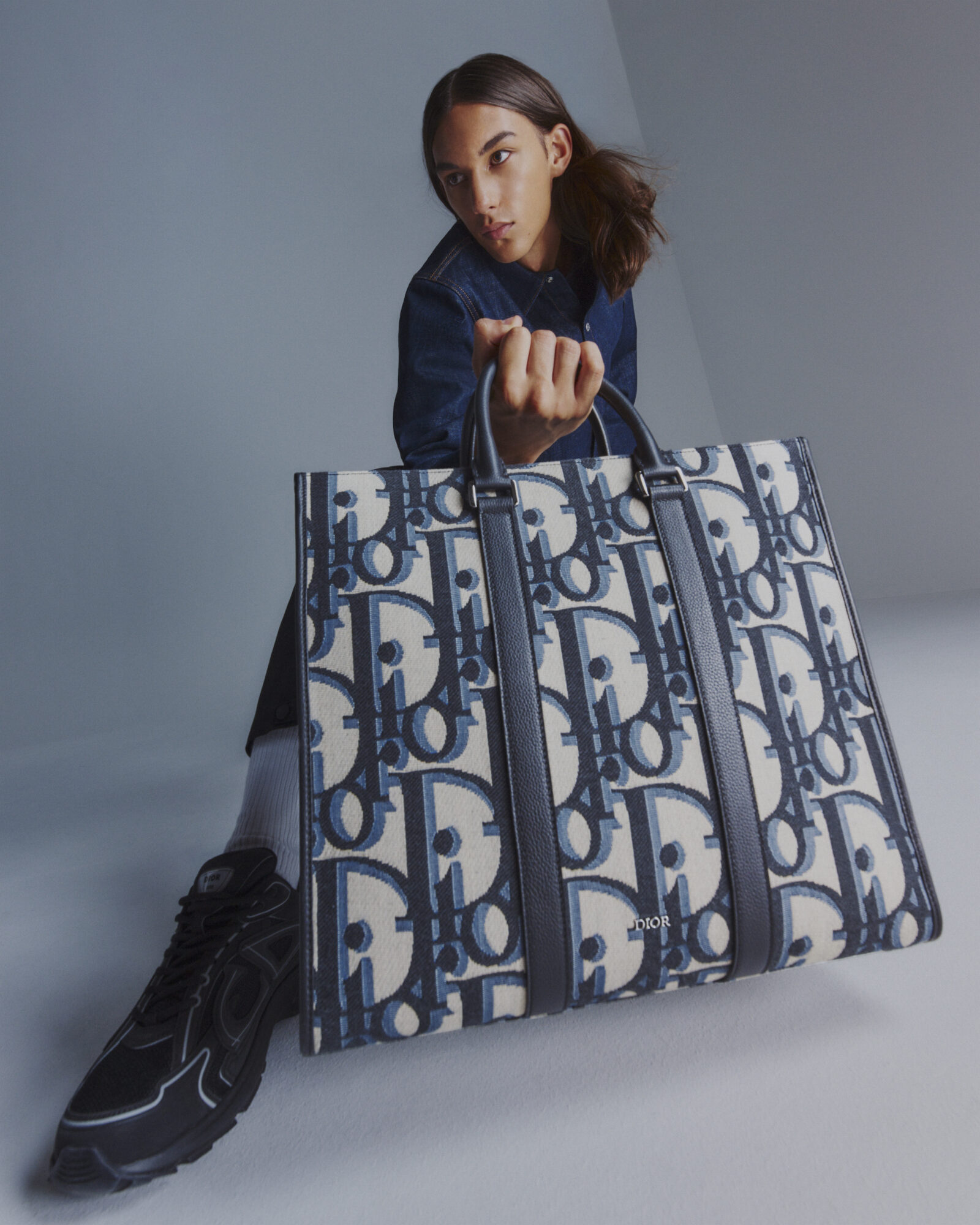 A close-up of the intricate Maxi DIOR Oblique pattern on a handbag, with the model's intense gaze adding a touch of drama.