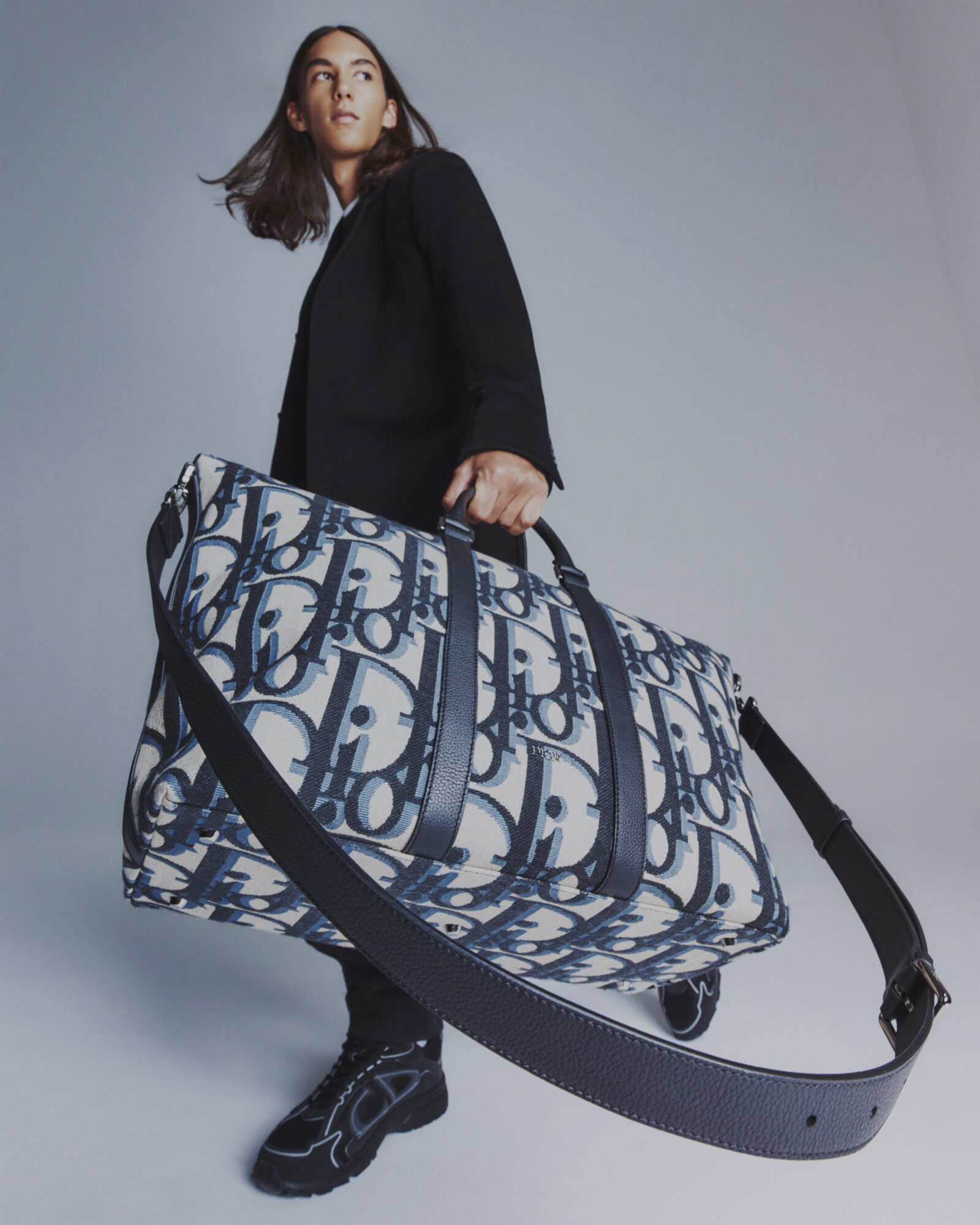 Showcasing effortless style, the model carries a spacious DIOR duffel bag - the epitome of luxury travel.