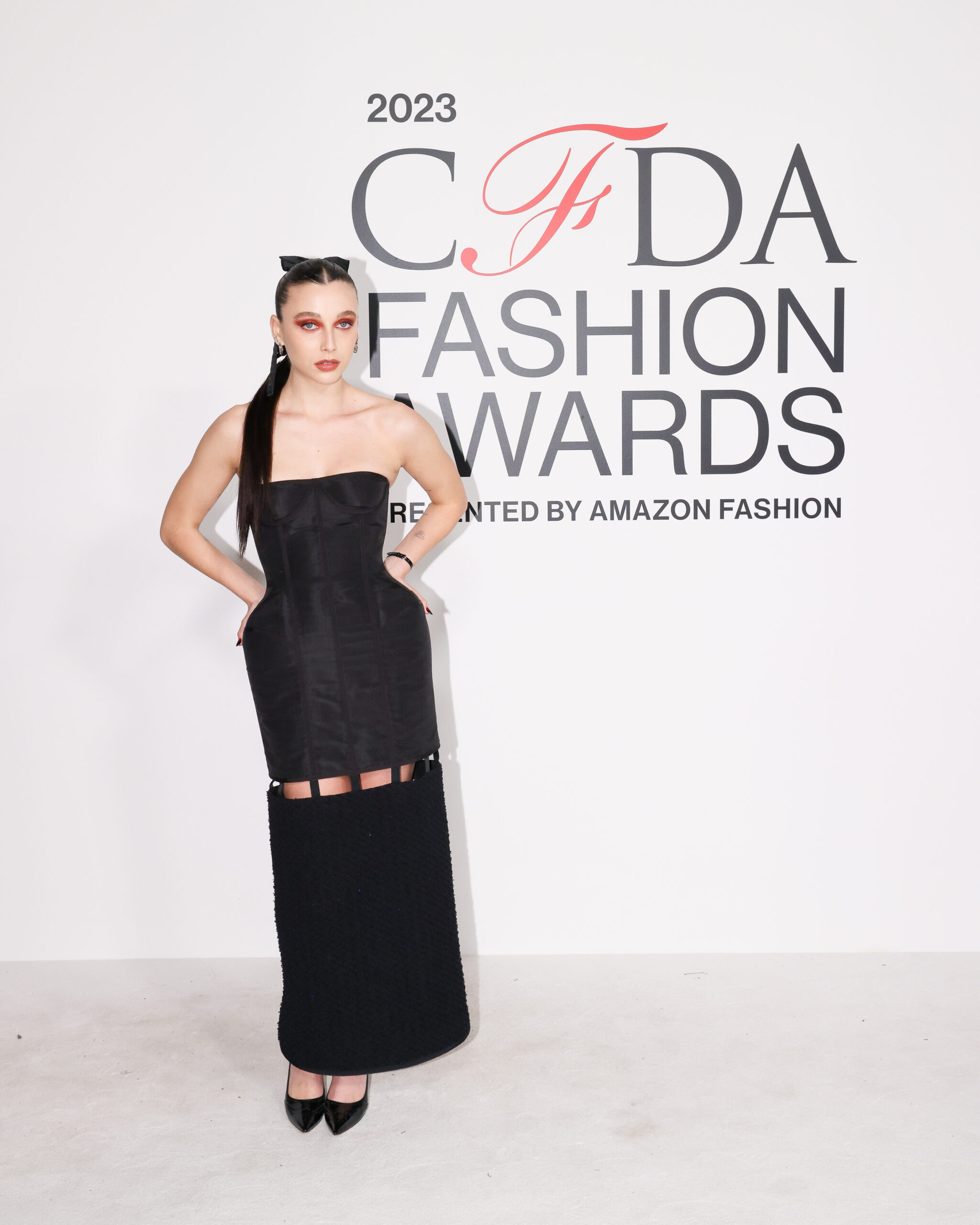 Emma Chamberlain strikes a pose at the CFDA Fashion Awards 2023, showcasing the bold elegance of a Thom Browne structured corset dress, complemented by a sleek hairstyle and statement makeup.