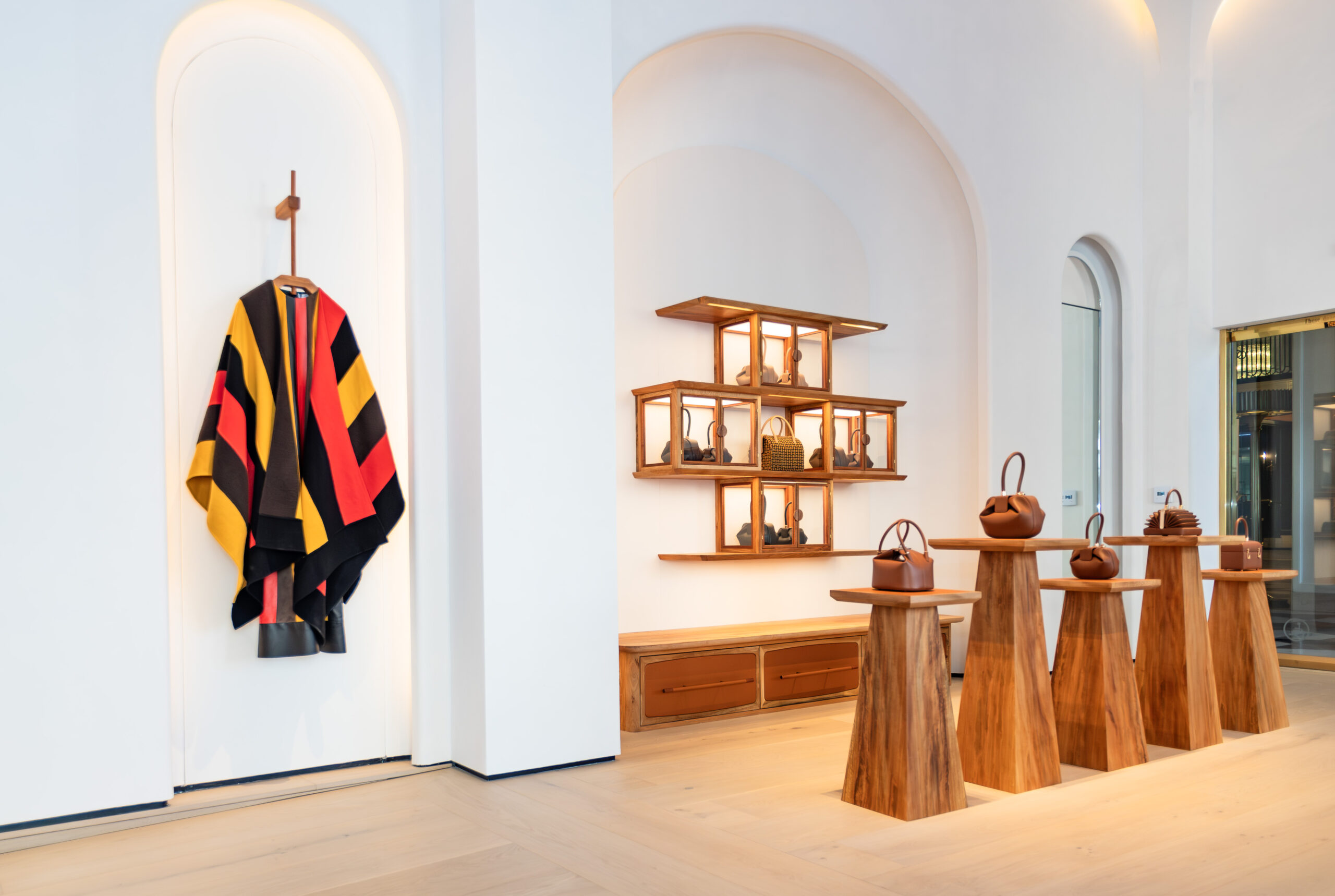 The interior of Gabriela Hearst’s flagship store in Beverly Hills showcases a blend of modern minimalism and artisanal warmth, featuring bespoke Nomad furniture pieces by Gavron Dumas Studio, constructed from locally sourced Western Sycamore timber. Handcrafted wooden tables with an organic form display the brand's exclusive handbag collection, while a wall-mounted shelving unit presents additional merchandise, all set against the backdrop of the store's elegant Roman Clay vaulted ceilings.