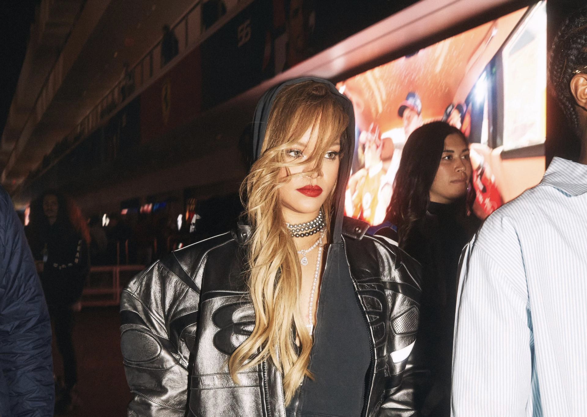 Rihanna commands attention in a silver jacket, black hoodie, and leggings, accented by a sparkling choker and bold red lipstick, embodying Puma's fusion of high fashion with streetwear aesthetics.