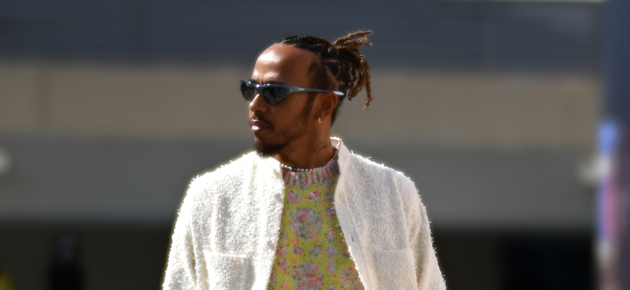 Lewis Hamilton walks in the Paddock at the Abu Dhabi Grand Prix, wearing a cream cardigan, floral turtleneck, and neon green sneakers.