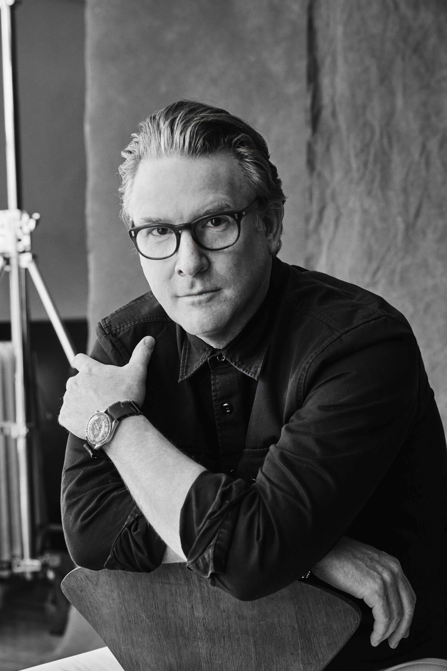 A black and white portrait of Todd Snyder with glasses, wearing a dark shirt and a watch, resting his chin on his hand.