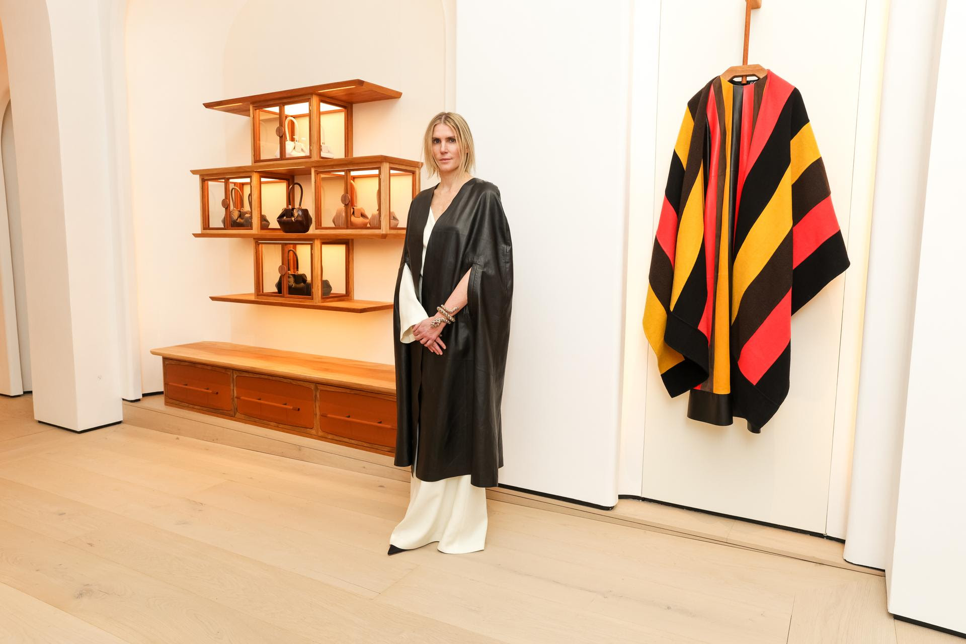 Gabriela Hearst stands with composed elegance in her new West Coast flagship store at the Beverly Wilshire, her presence as integral to the space as the sustainable luxury her brand is known for. Behind her, the artisanal wooden shelving displays her handbag collection, exemplifying the store's commitment to craftsmanship and quality. A strikingly colorful garment hangs to the right, providing a vivid contrast to the store's serene and polished interior.



