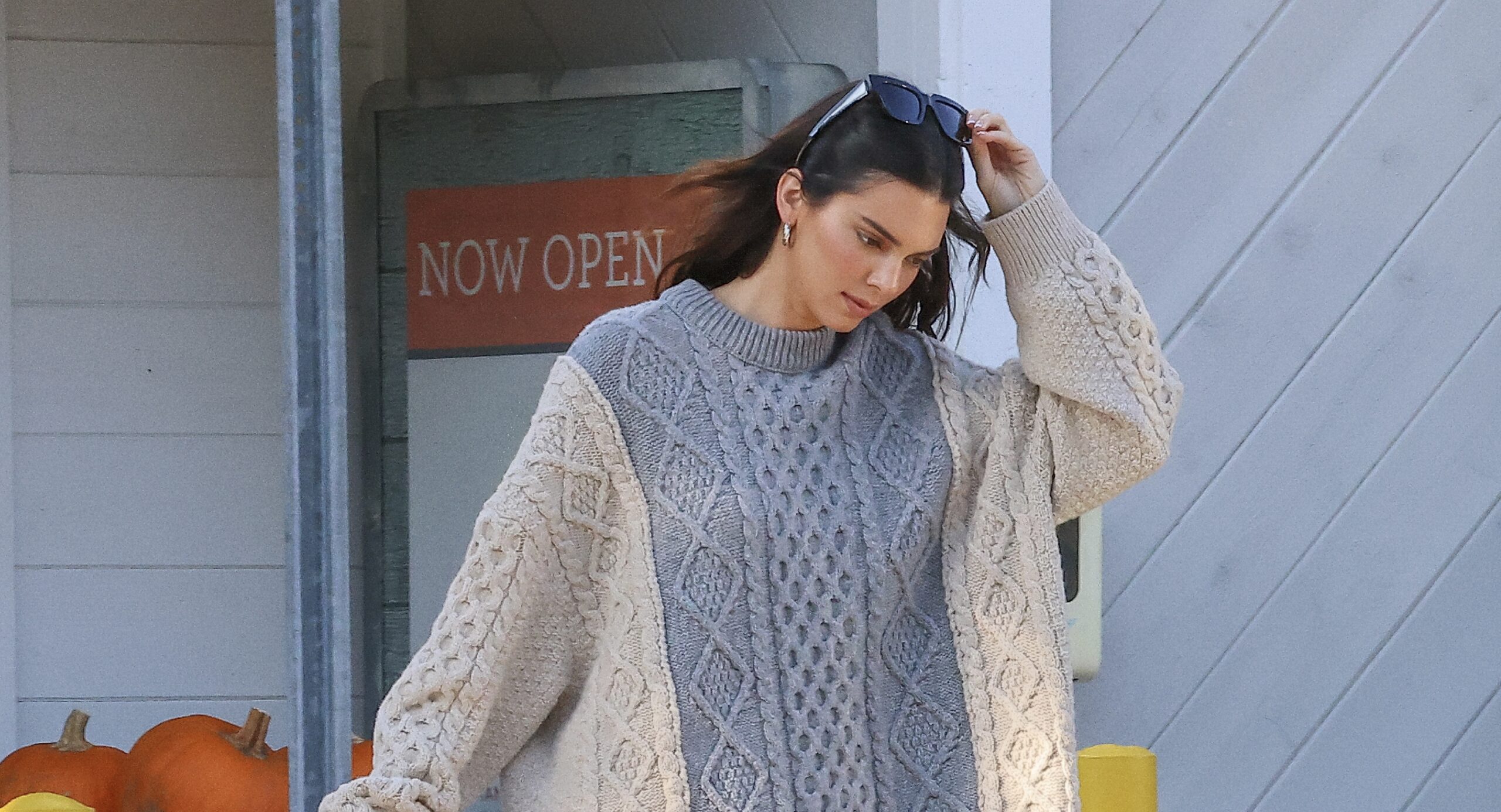 Kendall Jenner stepping out in a chunky knit sweater by Bottega Veneta, carrying a large tote and a bouquet of sunflowers, showcasing a relaxed yet luxurious style.