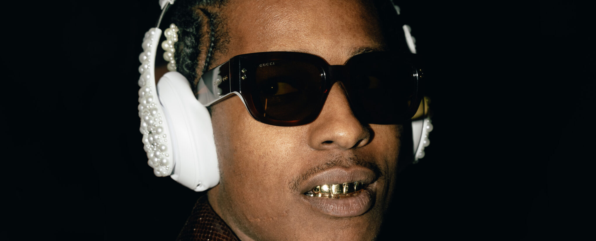 A$AP ROCKY wearing ornate Gucci sunglasses, embellished headphones, and a textured jacket with a snake skin pattern posing for a photograph.