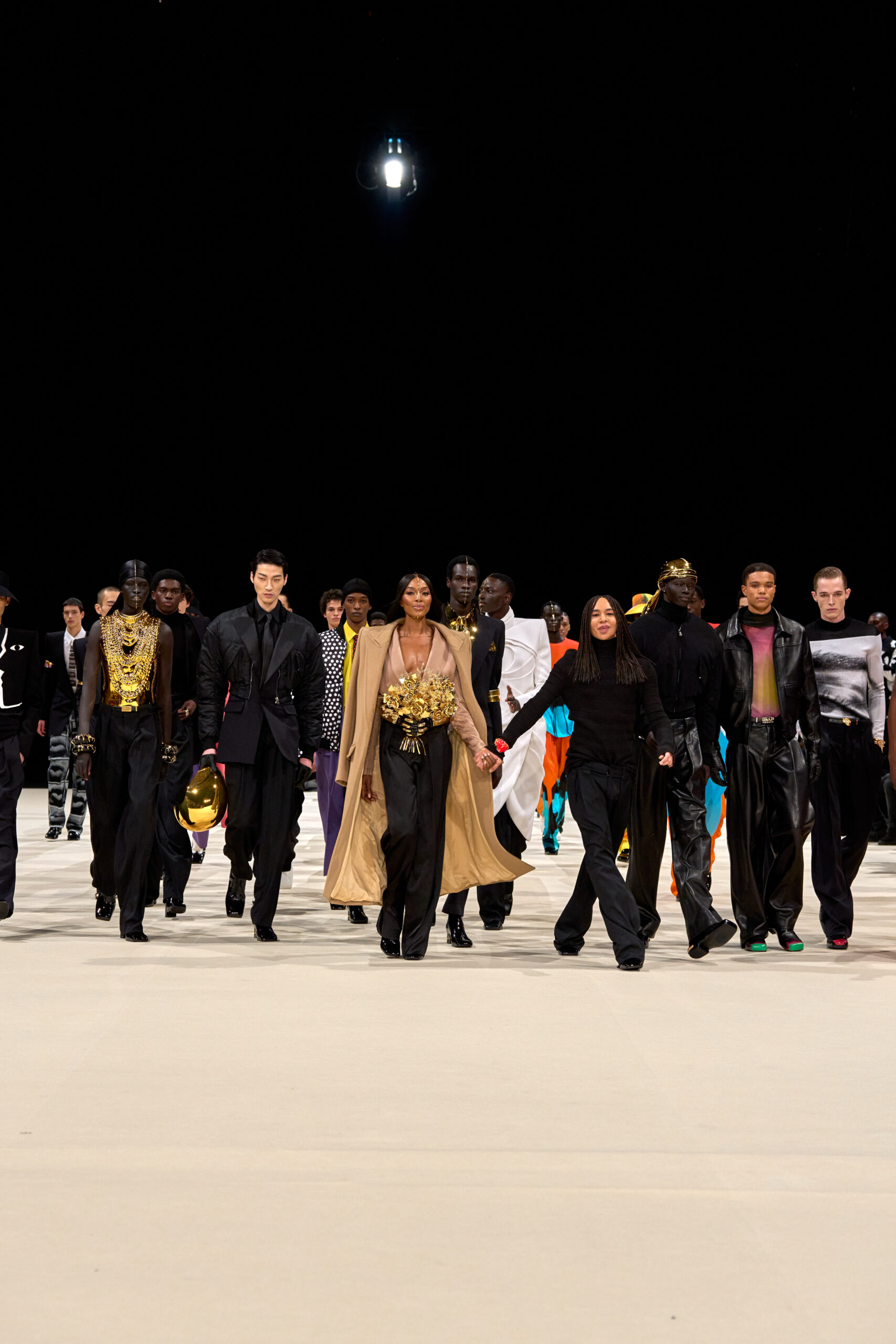 Naomi Campbell leading the finale walk at Balmain's Fall 2024 fashion show with a lineup of models showcasing a fusion of extravagant golden outfits and contemporary styles.