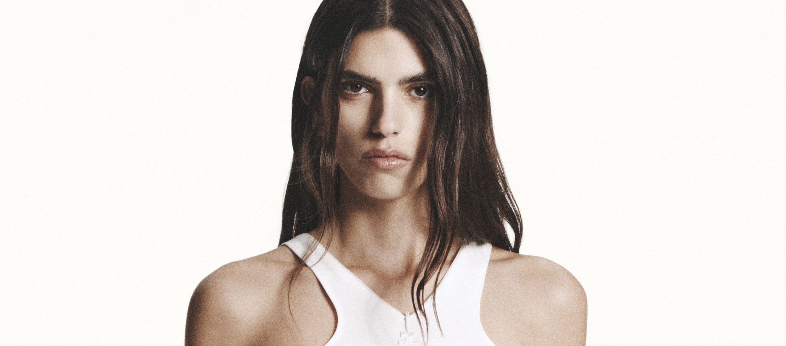 A model wearing a white sleeveless top from Courrèges Fall/Winter 2024 collection stands against a neutral background, exuding a minimalist and modern vibe.