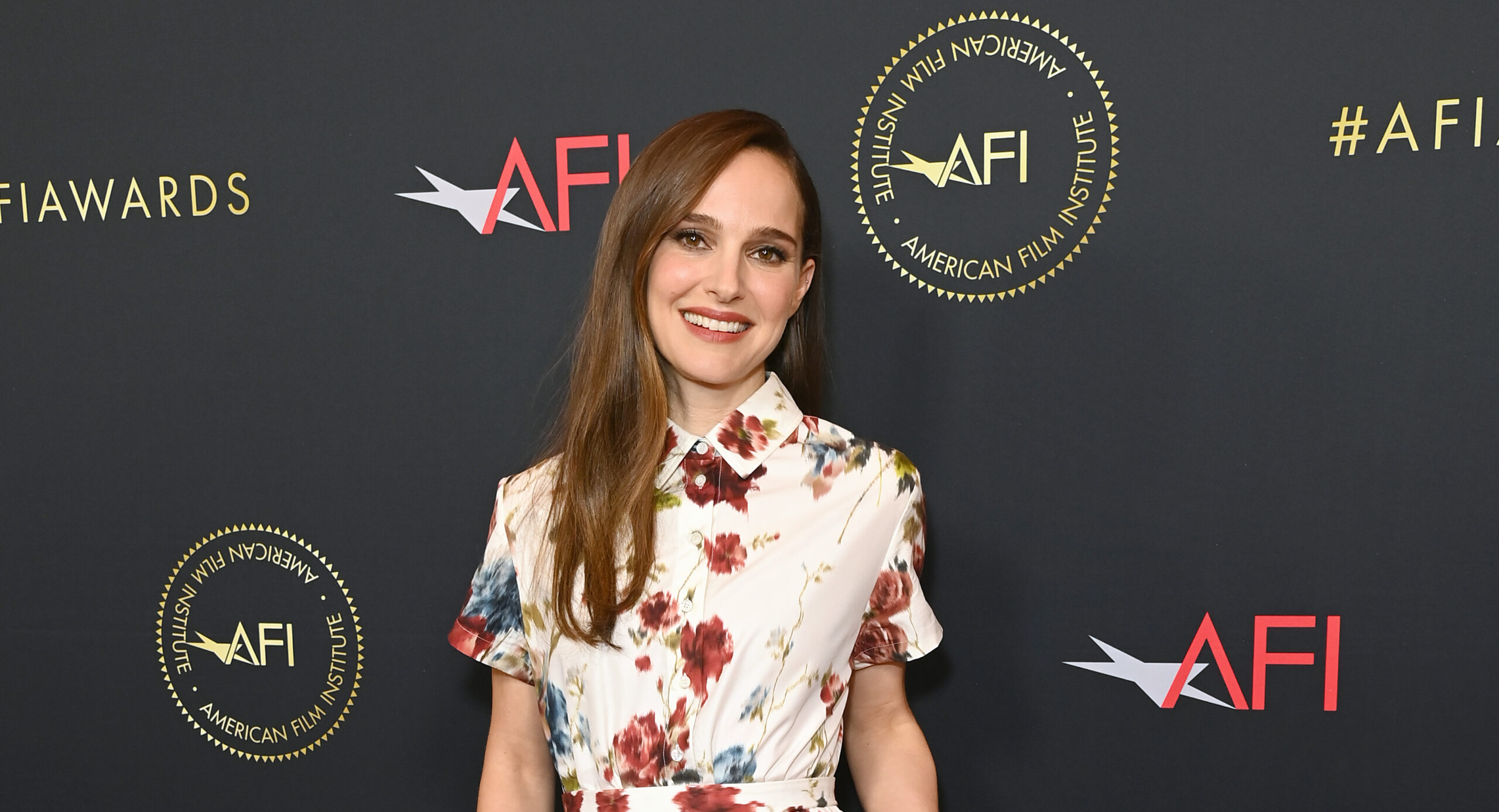 Natalie Portman in a floral Dior dress at the AFI Awards, her smile as captivating as her attire against the event's branded backdrop.