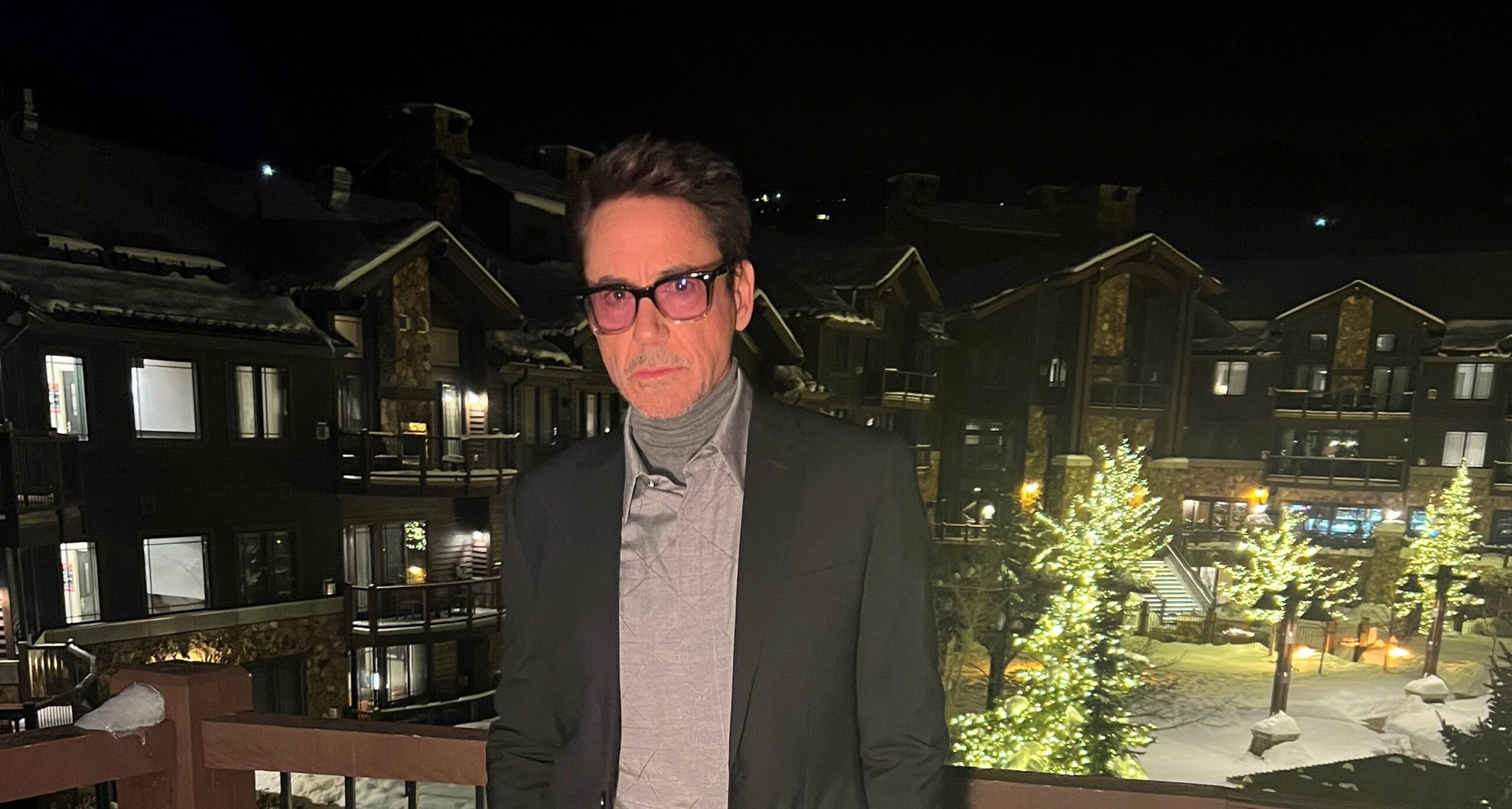 Robert Downey Jr. dressed in Dior at the Sundance Film Festival, posing on a balcony with a snowy evening backdrop.
