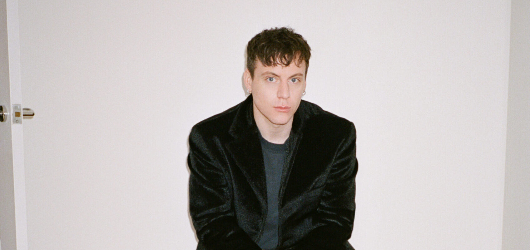Portrait of Sean McGrir, with a contemplative gaze, wearing a black velvet blazer over a casual shirt, set against a clean, white background.