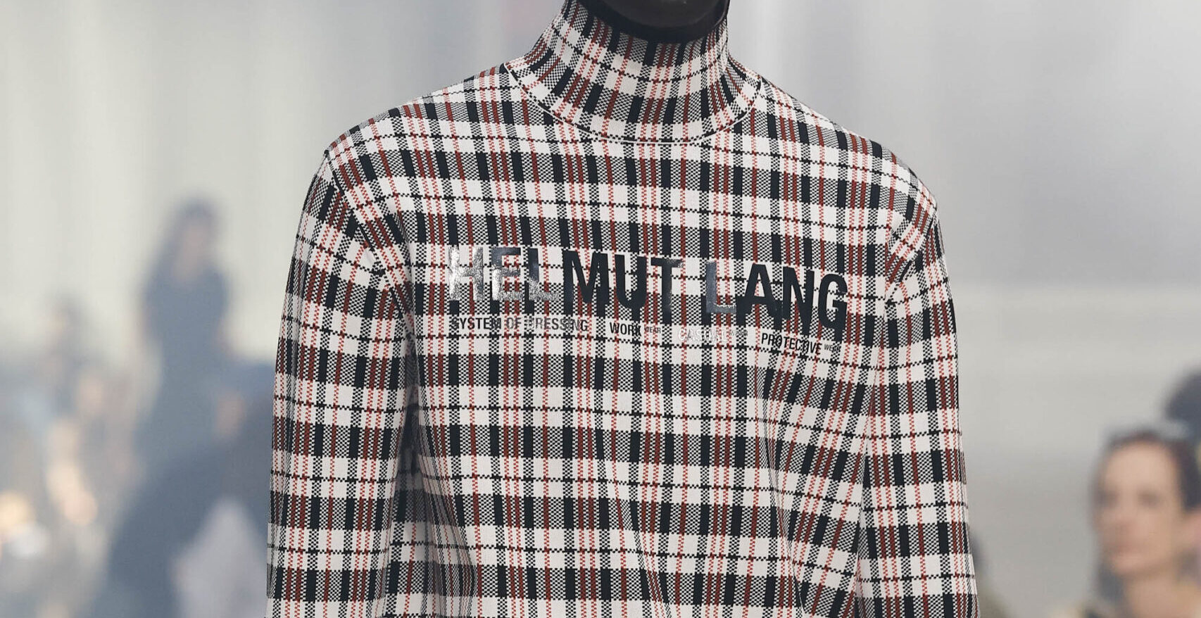Close-up of a model in a high-neck plaid garment with the text 'HELMUT LANG' from the Fall/Winter 2024 collection.