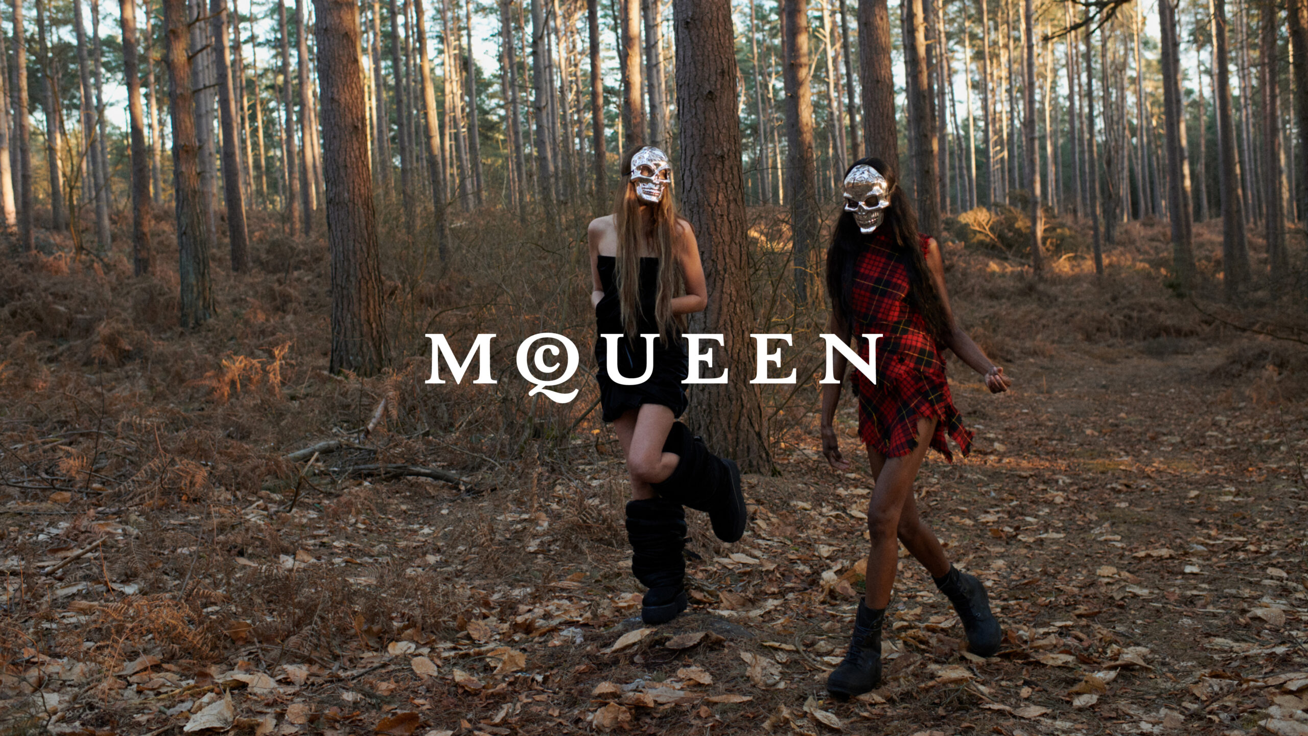 Two models in a forest, both wearing skull masks and stylish outfits, with the word "McQueen" in large, serif font at the center.