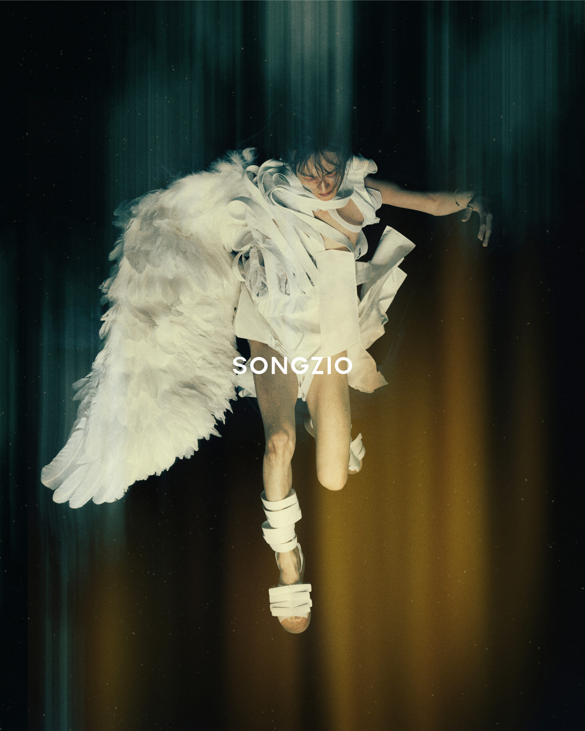 An artistic image featuring a figure adorned with white feathered wings and textured garments, suspended in mid-air against a backdrop of dark vertical streaks and golden light, with "SONGZIO" written at the bottom.