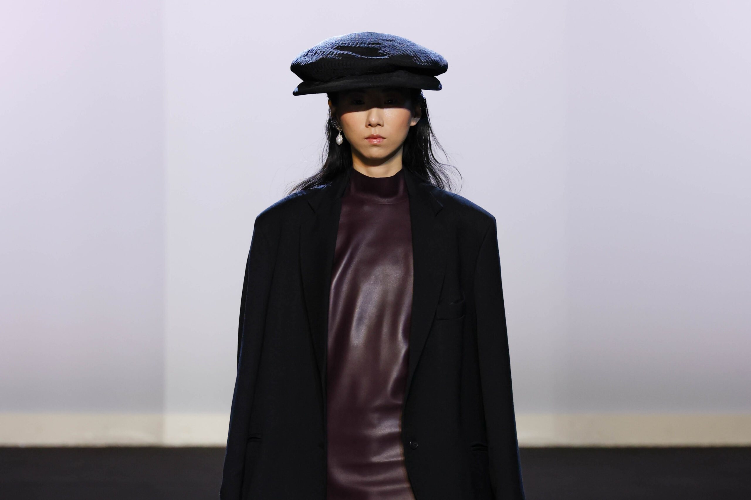 A model at Milan Fashion Week is clad in an Alberto Zambelli 'Nexum' Fall/Winter 2024 collection piece, featuring a sleek maroon turtleneck and a classic black blazer. The ensemble is accessorized with a textured black beret and simple yet elegant pearl earrings, presenting a chic and modern look.