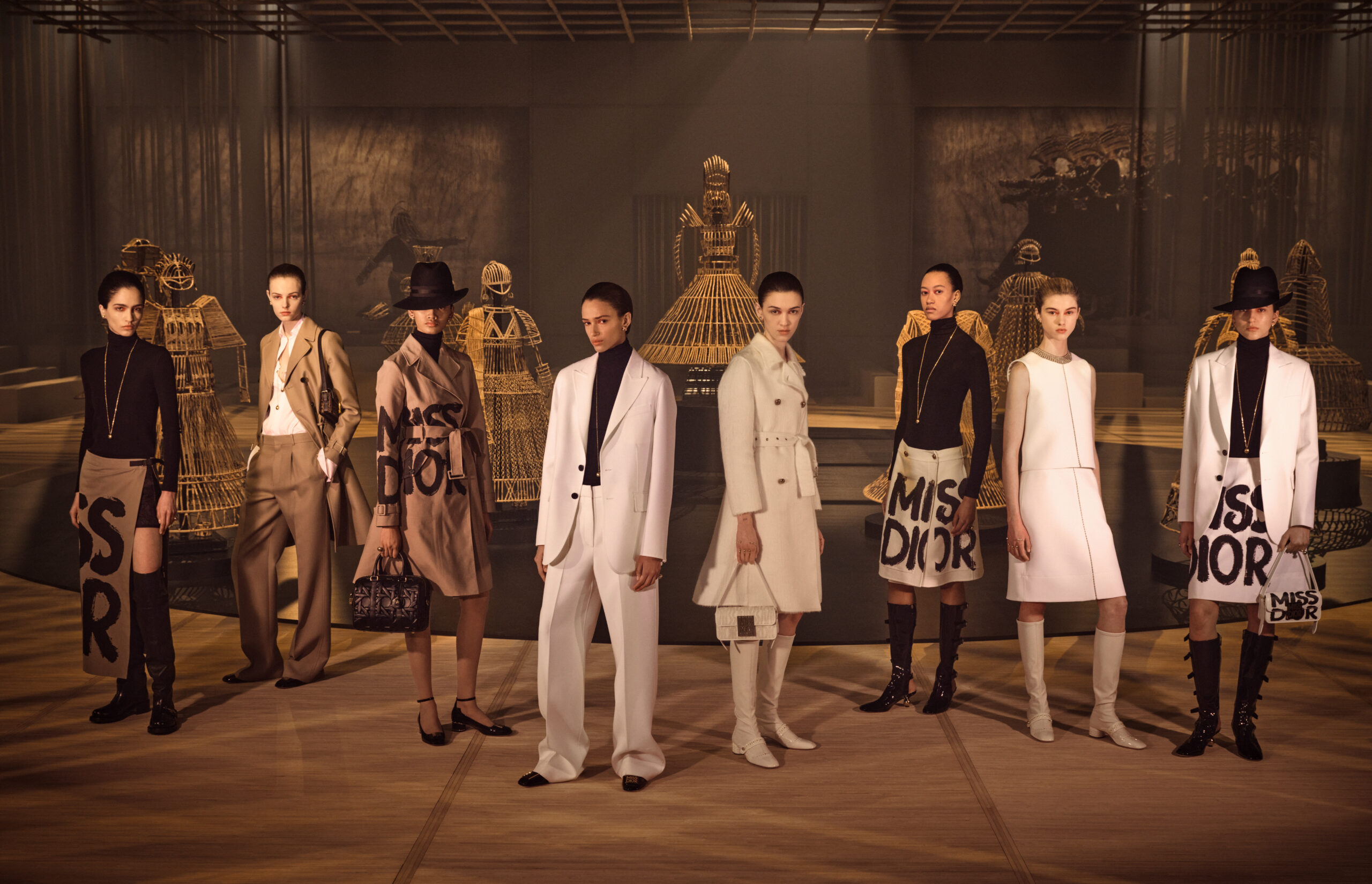 A line-up of models in Dior's latest collection, with cane art sculptures in the background on a fashion show runway.