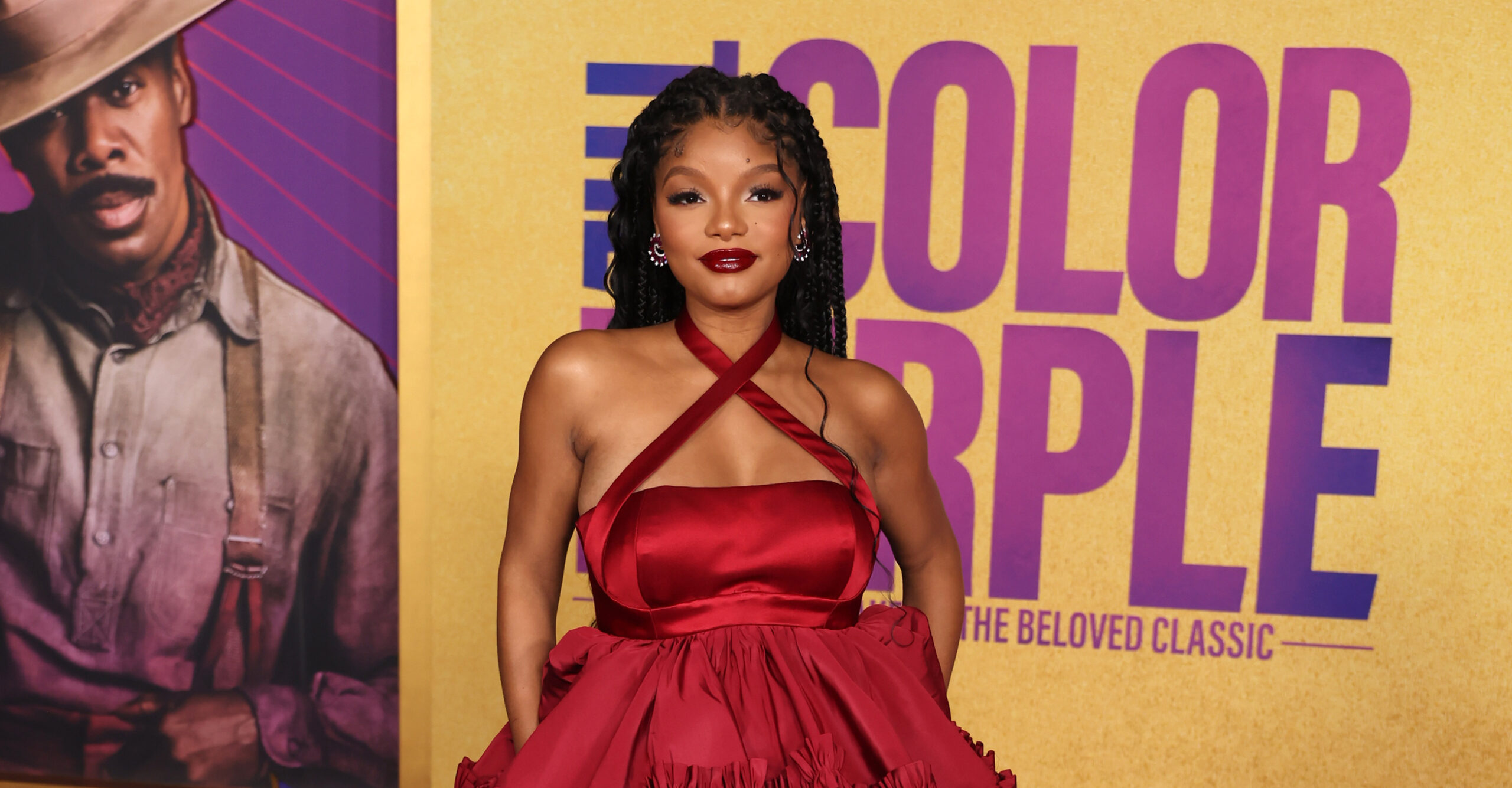 Halle Bailey stands confidently on a purple carpet at the Los Angeles premiere of "The Color Purple," wearing a breathtaking Off-White™ red ruffled gown.