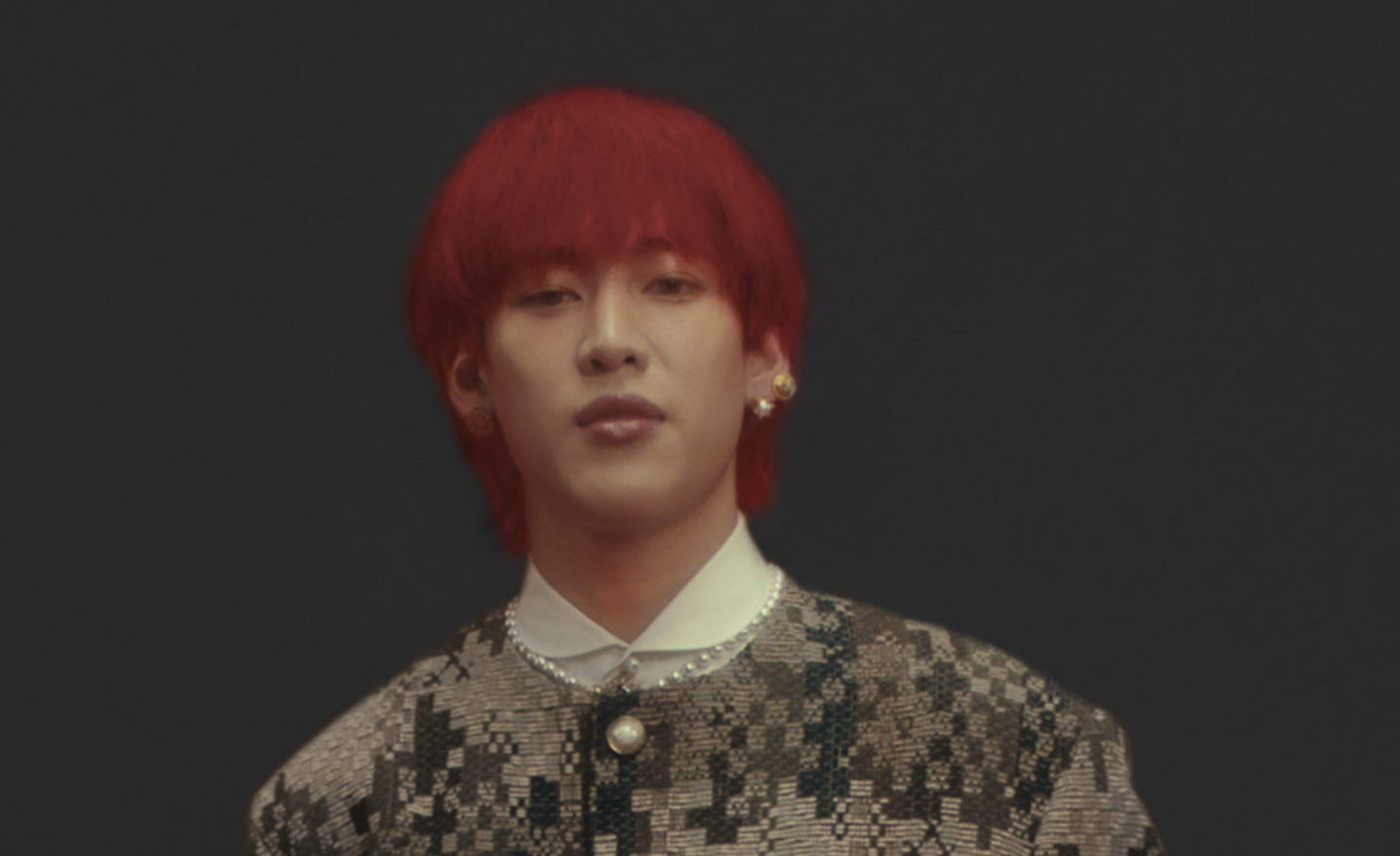 BamBam, with vibrant red hair, clad in a pixel-patterned Louis Vuitton jacket, exudes contemporary style.