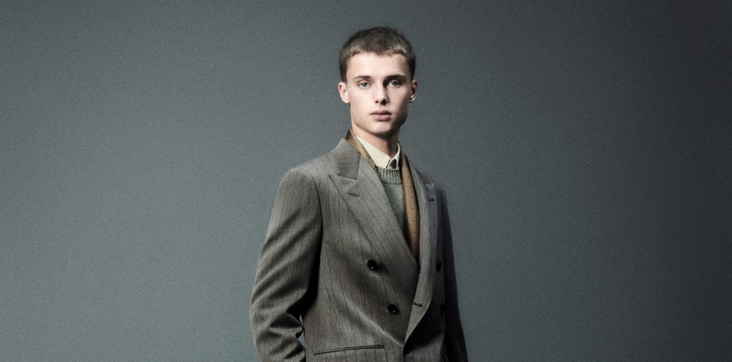 A model poses in a classic double-breasted blazer over a light olive turtleneck from Loro Piana's Fall/Winter 2024-2025 collection, capturing an essence of timeless menswear.