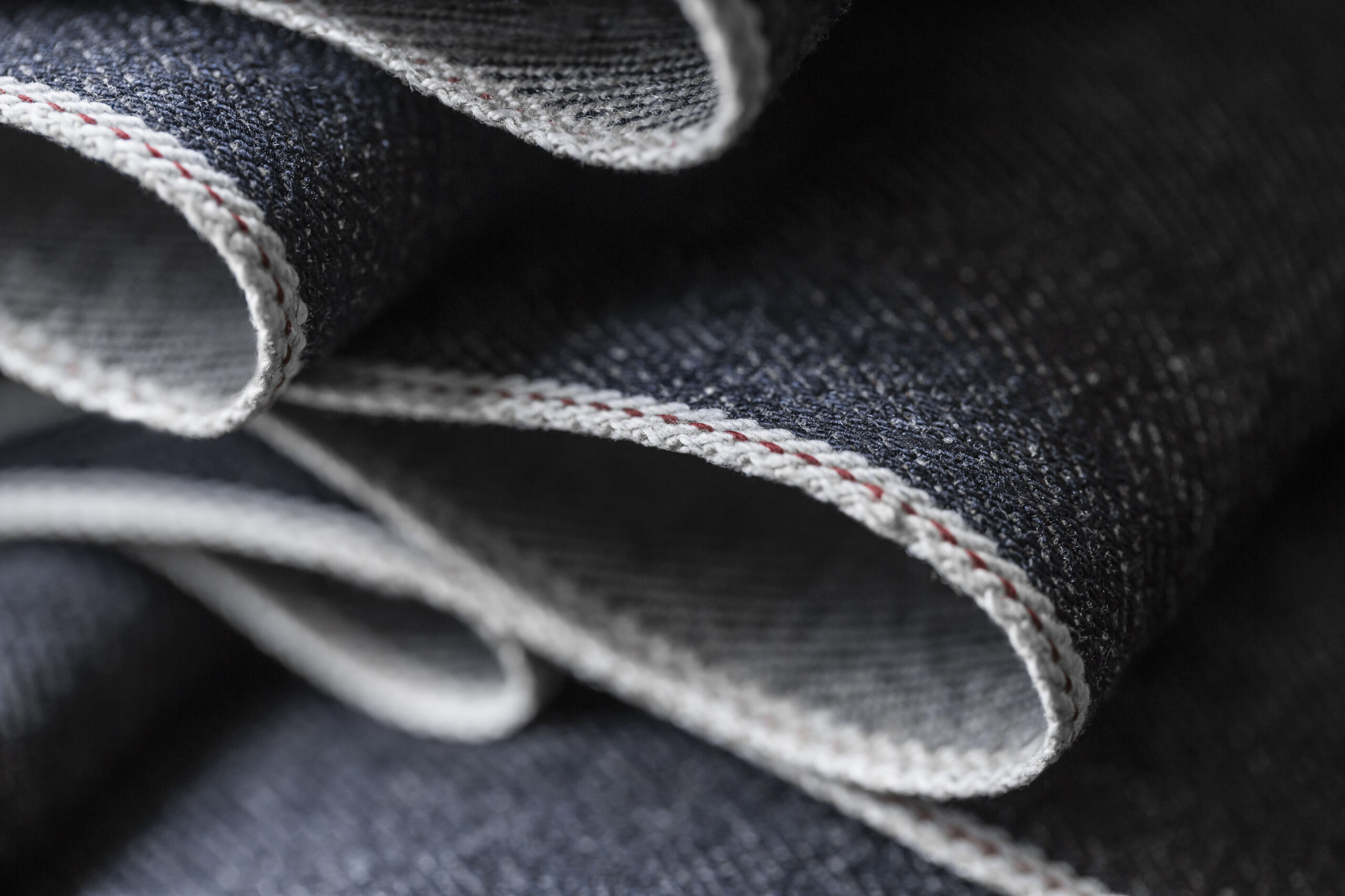 Close-up of a luxurious CashDenim® fabric showcasing the detailed twill weave and signature red and white selvedge edge, exemplifying the blend of traditional craftsmanship and innovation.