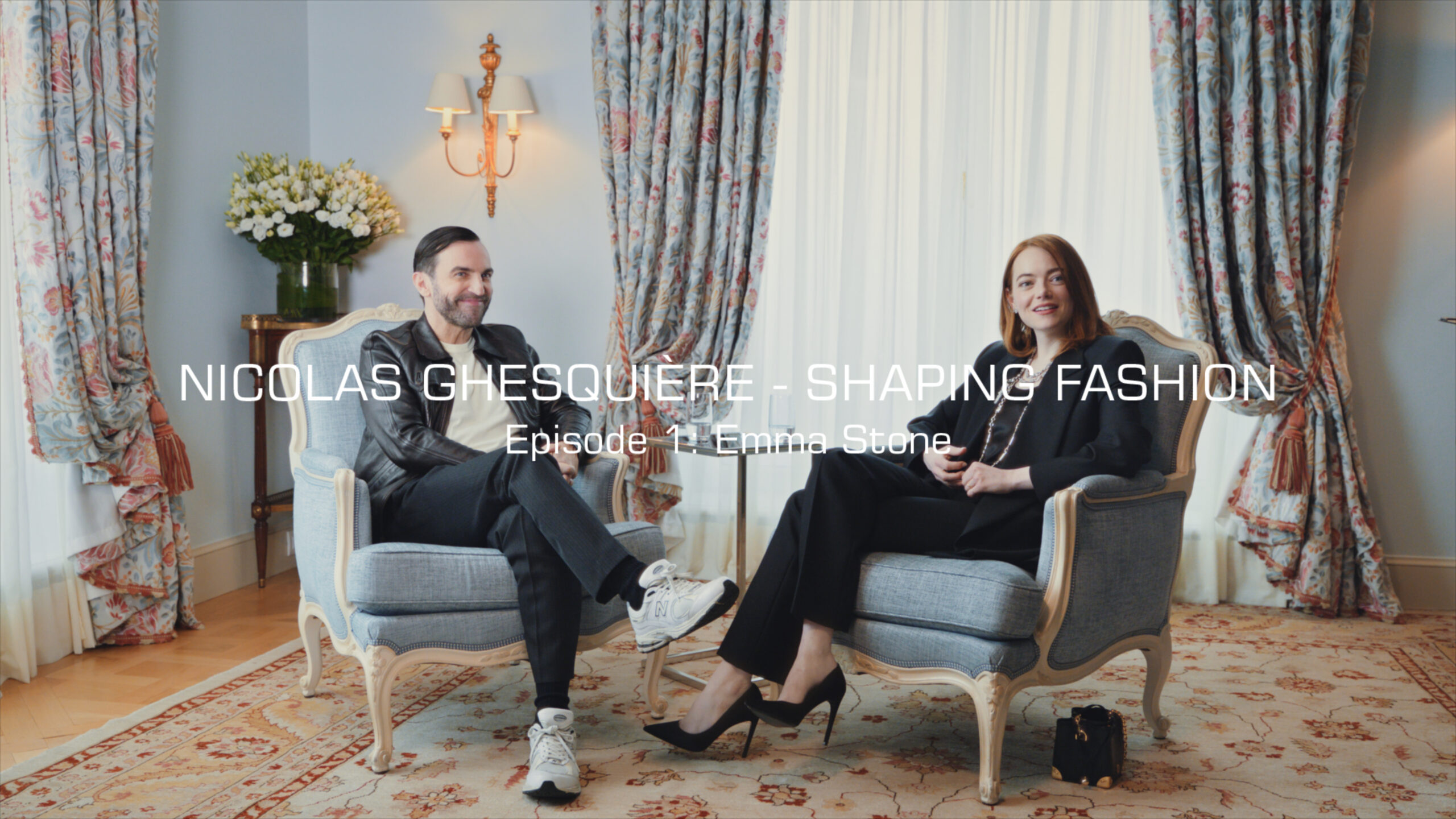 Nicolas Ghesquière and Emma Stone seated in an opulent room, engaged in conversation for the YouTube series 'Nicolas Ghesquière - Shaping Fashion'.