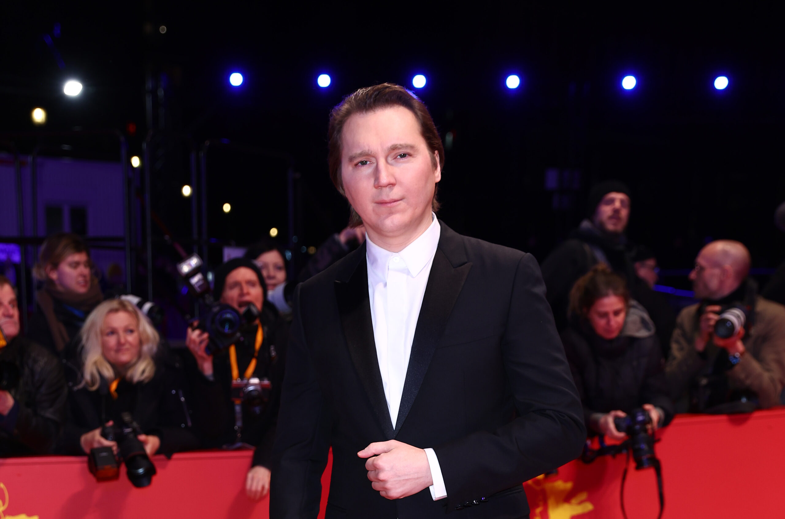 Paul Dano stands on the red carpet at the Berlin Film Festival, clad in a black wool and silk Dior tuxedo with a white cotton shirt, embodying elegance.