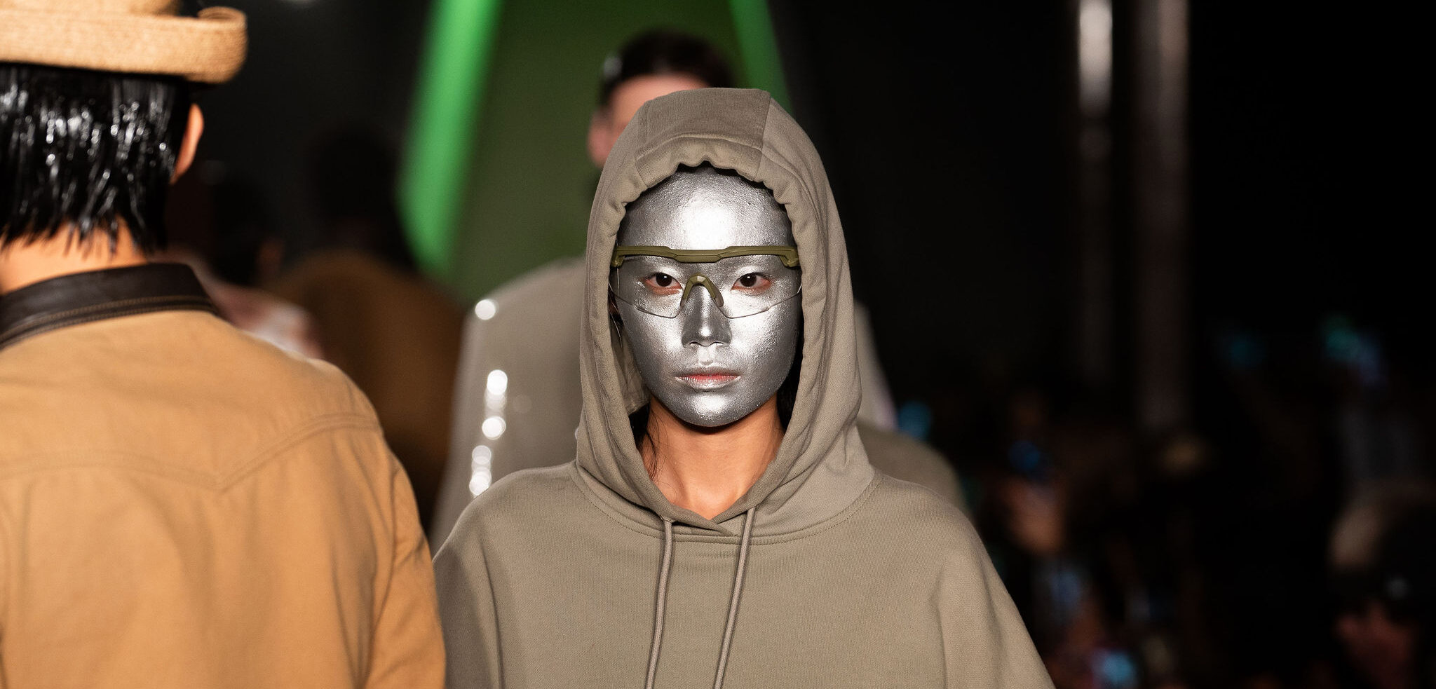 A model wearing a hooded garment with a metallic silver mask covering the face walks the runway at New York Fashion Week, reflecting PRIVATE POLICY's FW24 'Wild Wild World' collection theme that combines futuristic elements with Wild West inspirations.