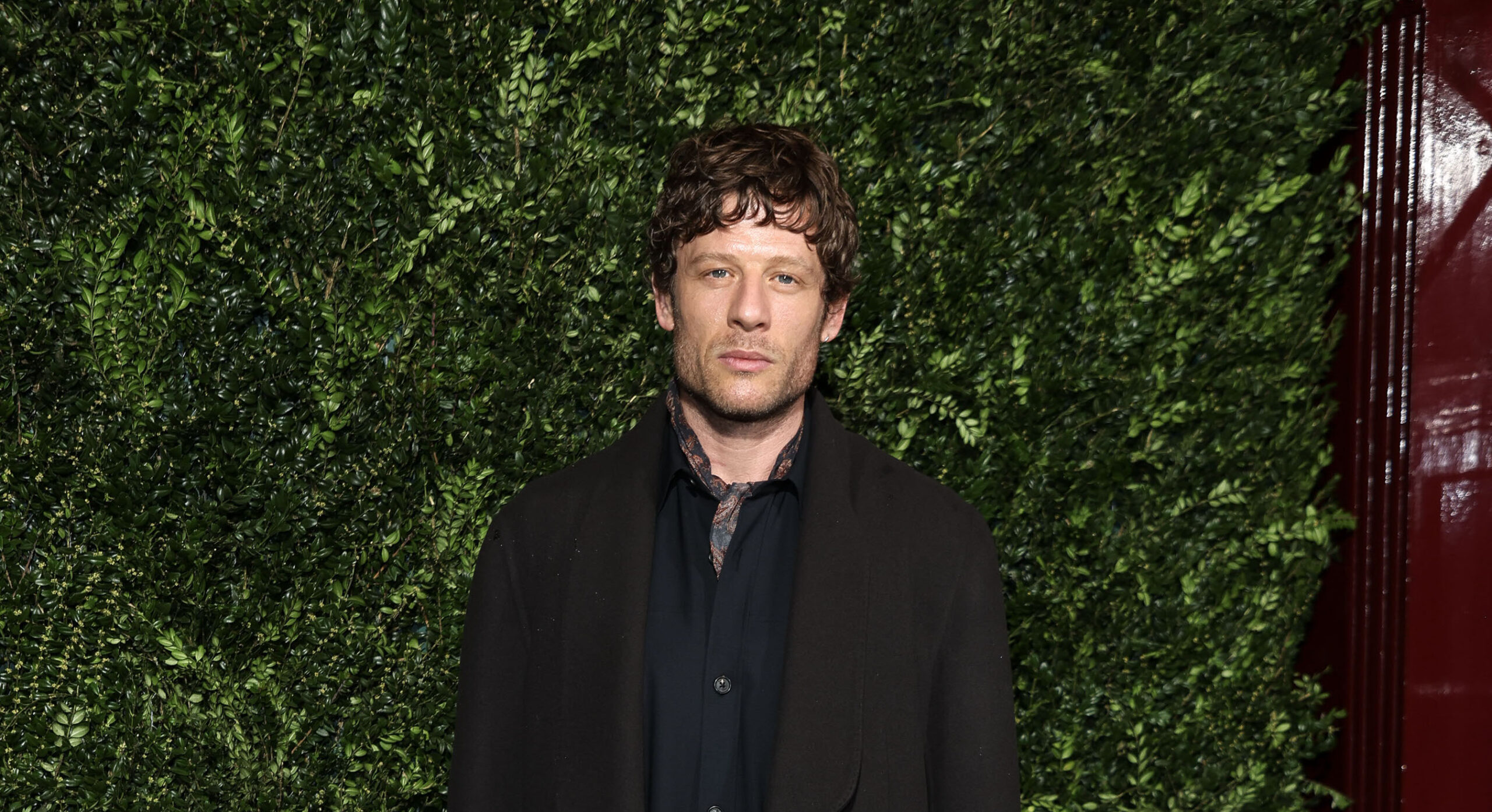 James Norton stands confidently at the Charles Finch & Chanel Pre-BAFTA Party in a dark chocolate wool cashmere coat from dunhill's Autumn Winter 2024 collection, with a navy paisley neckerchief adding a touch of artistry.