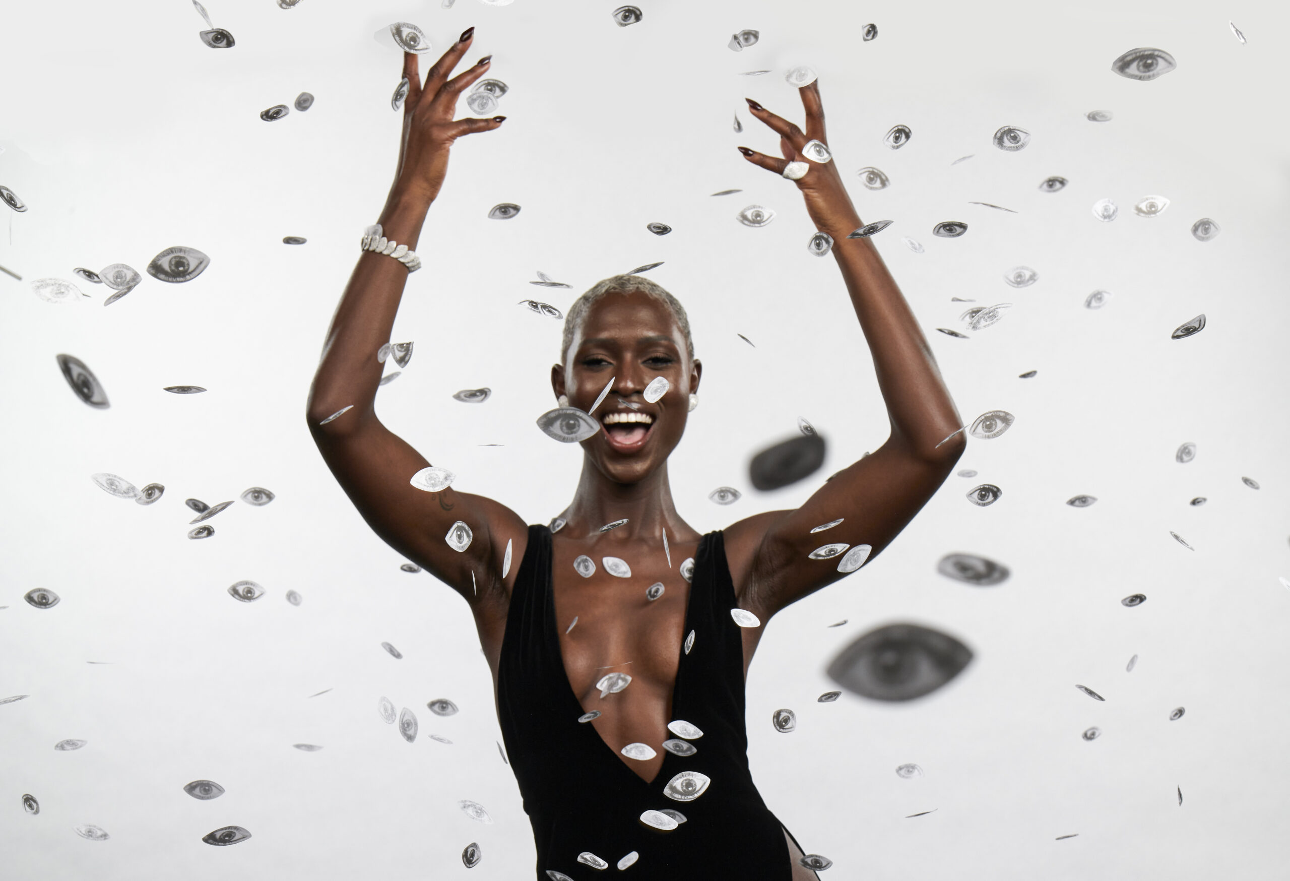 Jodie Turner-Smith joyously throws her arms up, surrounded by a shower of silver confetti coins, capturing a moment of celebration and exuberance at an Oscars' after-party.