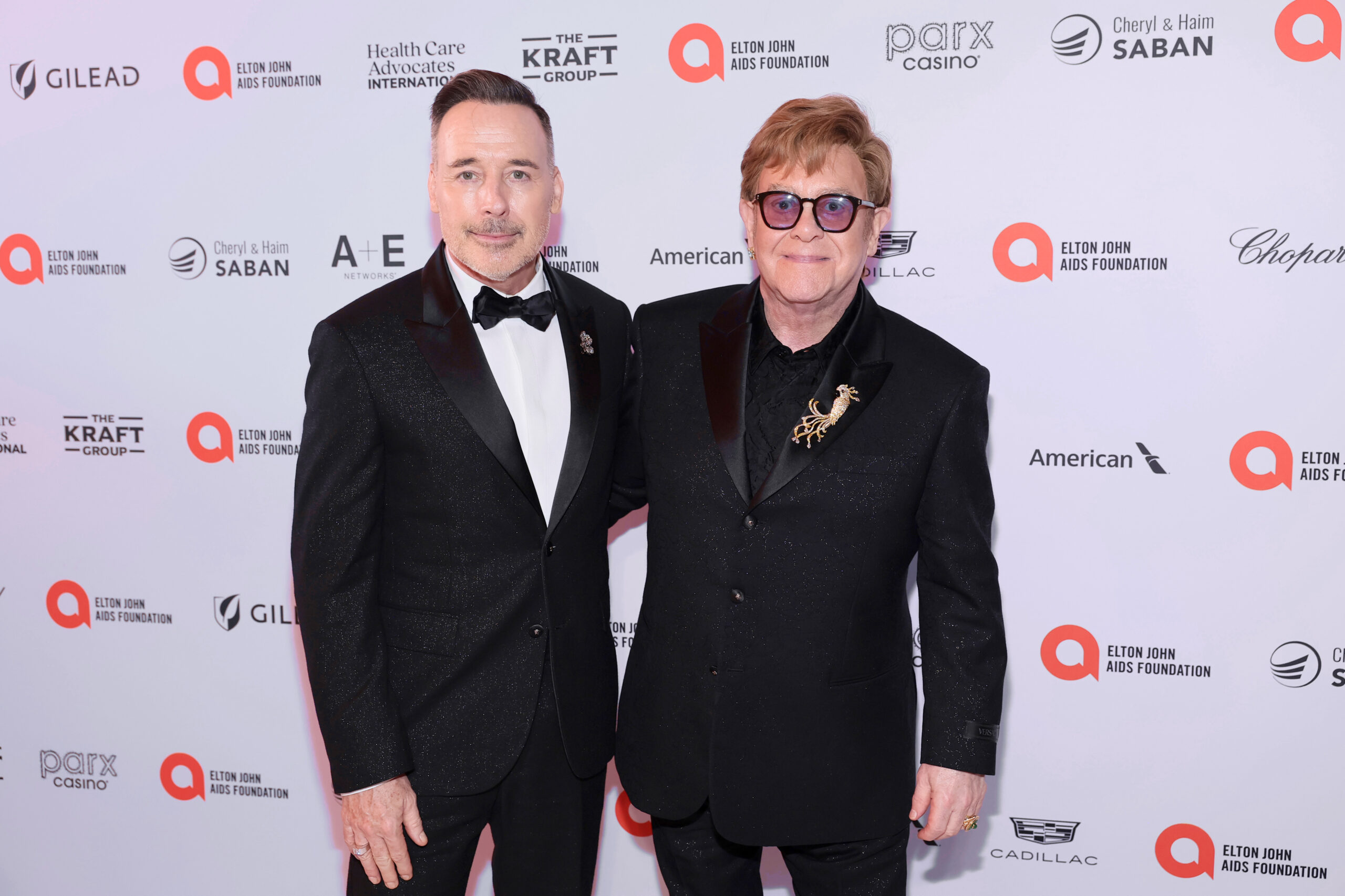 David Furnish and Sir Elton John pose together at the Elton John AIDS Foundation's 32nd Annual Academy Awards Viewing Party, held on March 10, 2024, in West Hollywood, California. Both are dressed in elegant Versace suits.