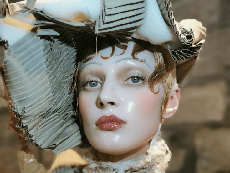 A close-up image of a model from Maison Margiela's Spring 2024 couture collection wearing a deconstructed headpiece, reminiscent of Galliano's dramatic and romantic vision.