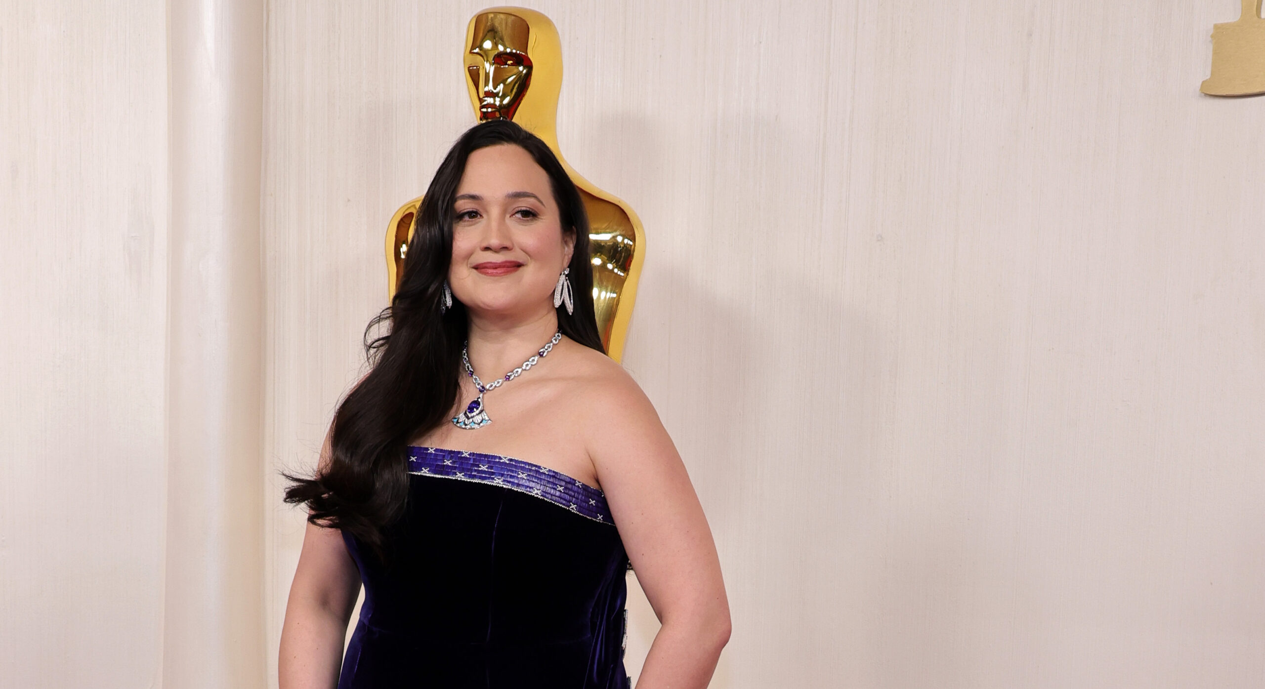 Lily Gladstone poses confidently at the 96th Annual Academy Awards, wearing a custom Gucci gown. The dress features a deep midnight blue color with a flowing train and is embellished with white quillwork patterns along the edges, celebrating her Indigenous heritage.
