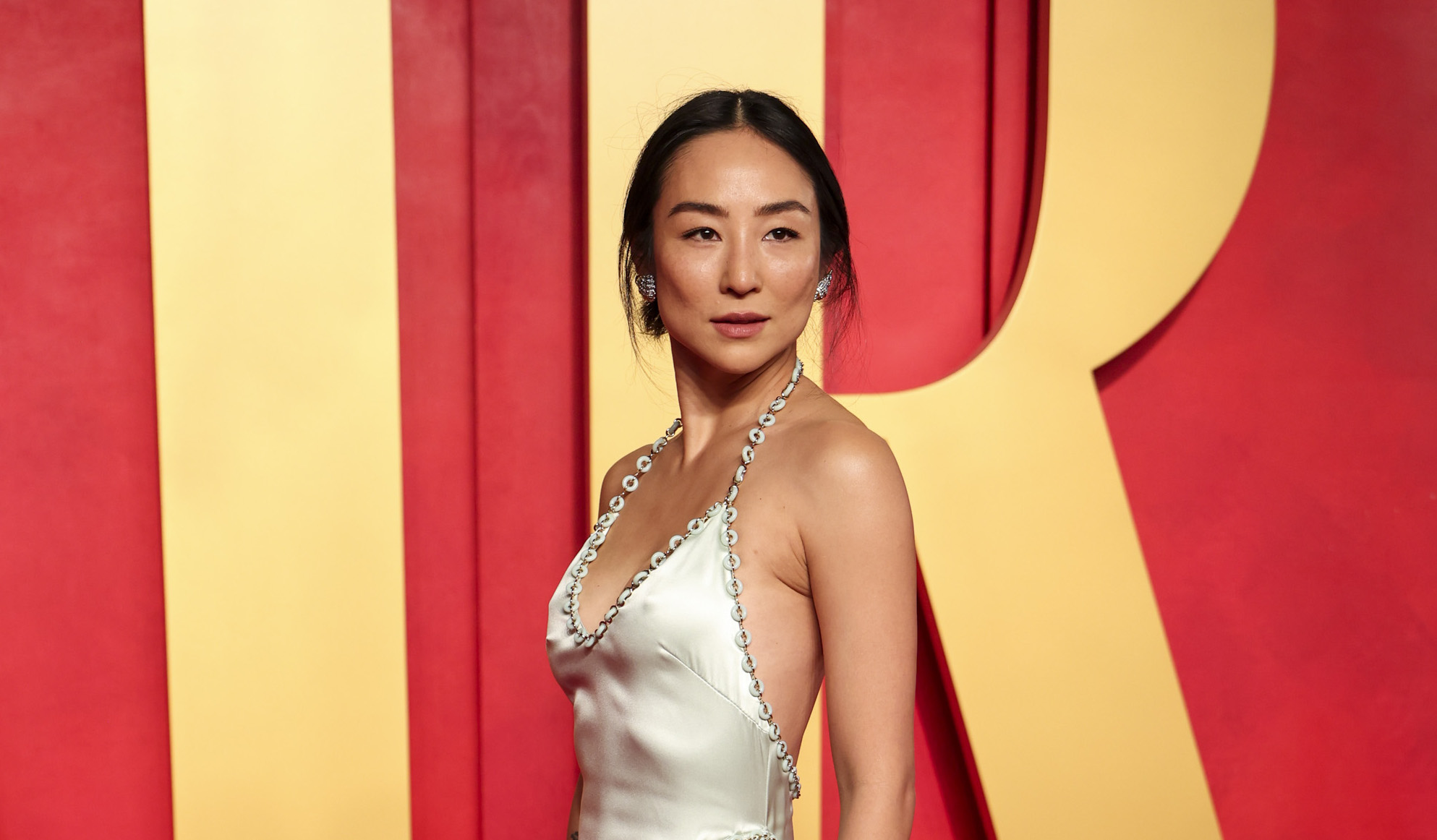 Greta Lee stands elegantly on the red carpet in a custom LOEWE silk satin halter neck dress at the 2024 Vanity Fair Oscar Party.