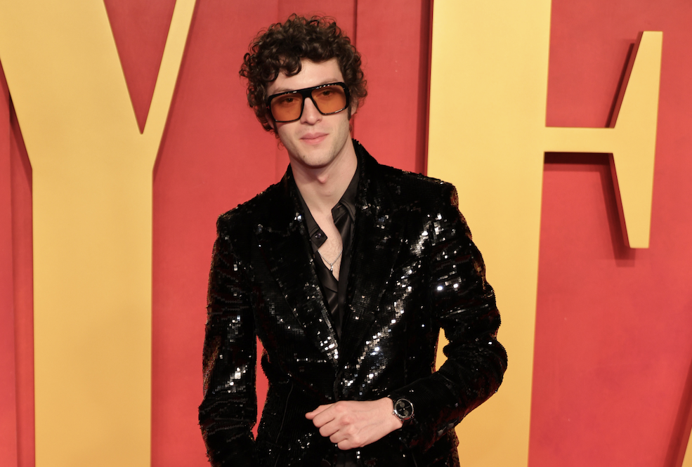 Dominic Sessa strikes a pose at the 2024 Vanity Fair Oscar Party, donning a Tom Ford black sequined jacket and orange-tinted sunglasses.