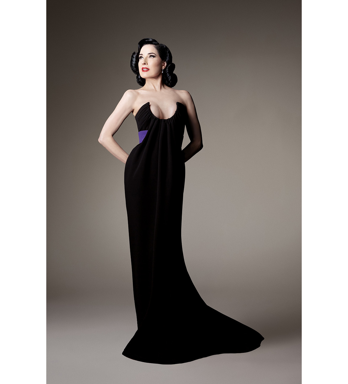 Look 1, Dita von Teese. Long bustier sheath dress in black crepe mousse, featuring a crescent-shaped neckline with draped pleats, cinched with violet satin (Photo: Courtesy of Alexis Mabille)