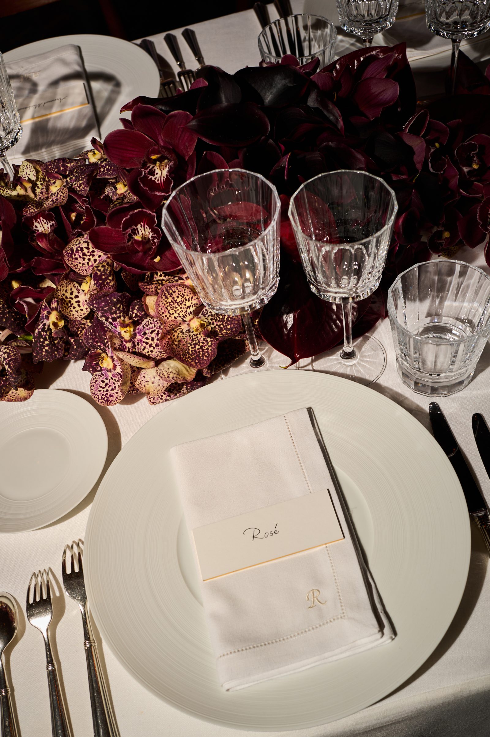 Rich burgundy orchids frame an elegant place setting at the Saint Laurent x Vanity Fair pre-Oscar dinner held in Mitch Glazer and Kelly Lynch's Hollywood Hills home.